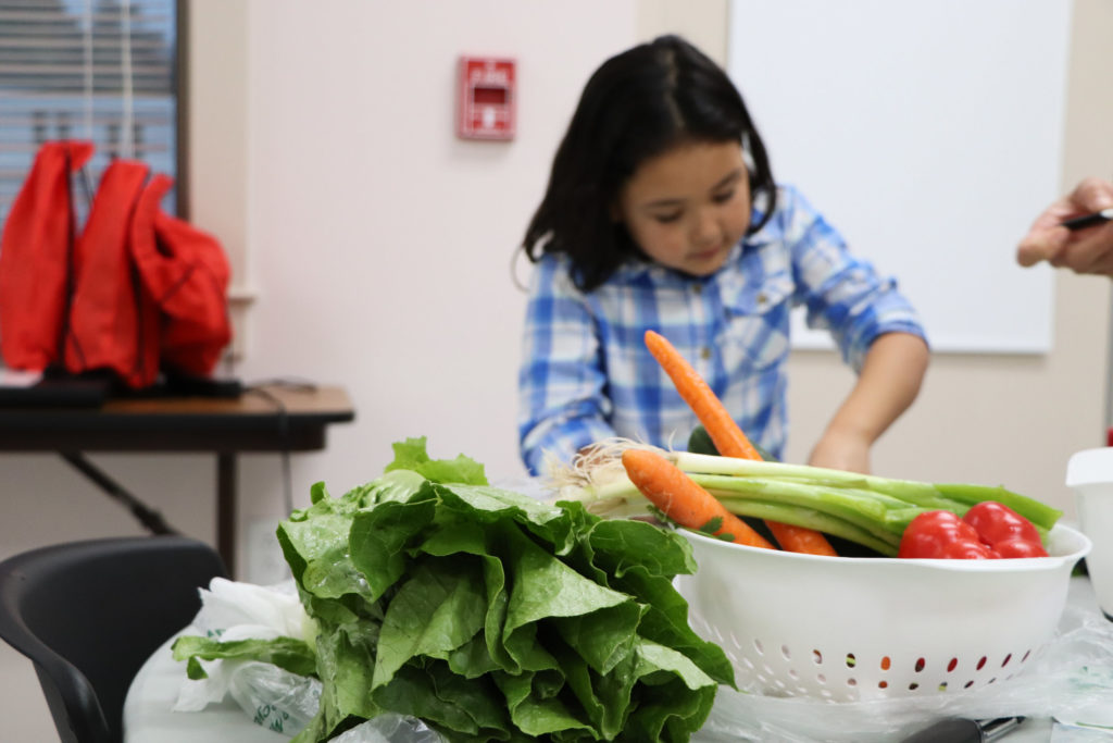 A girl cuts fresh produce at a Cooking Matters class.