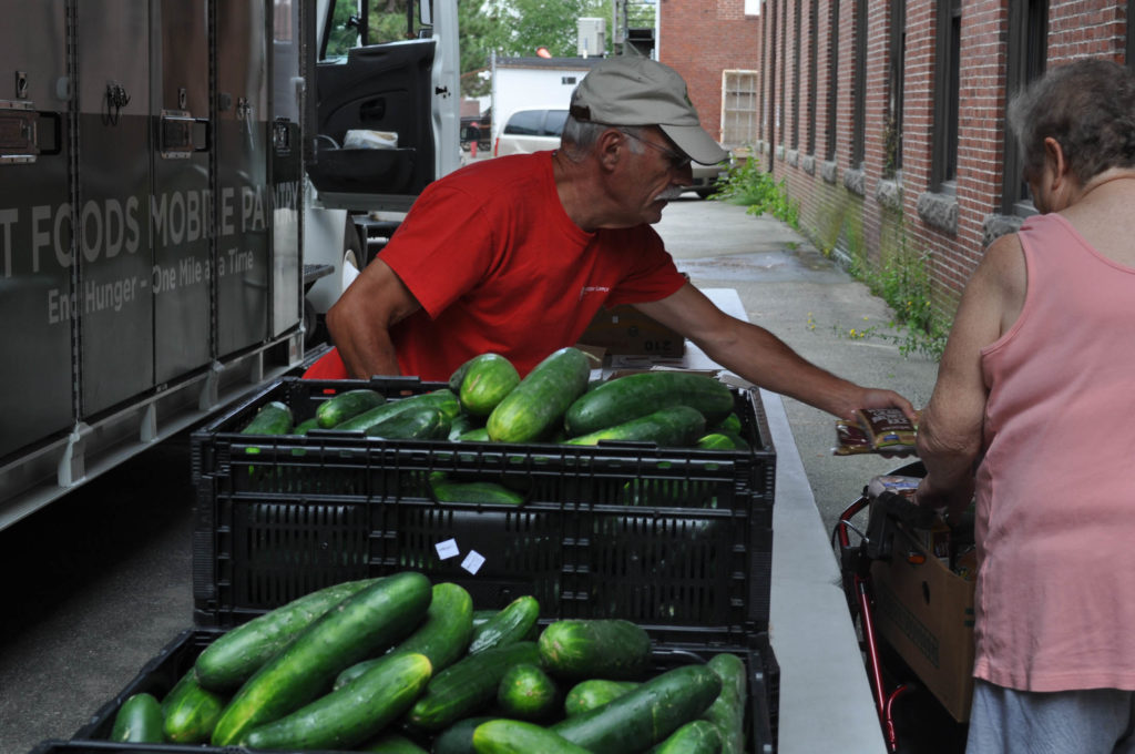 A volunteer gives cucumbers to a guest at the GSFB Food Mobile in Biddeford.