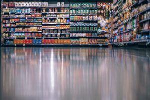 The stocked shelves of a grocery store are reflected on the clean floor.