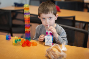 A young boy pauses building legos to sip on a carton of milk.