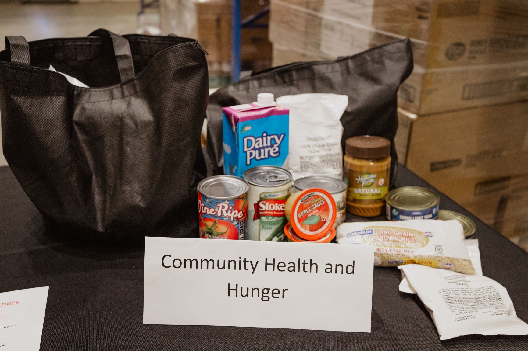 Community Health and Hunger's table display of healthy shelf-stable food and bags.