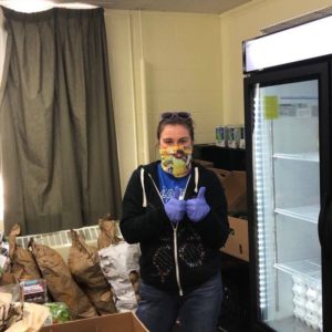 A Food AND Medicine volunteer gives two gloved thumbs up and smiles behind her mask at a local food pantry.