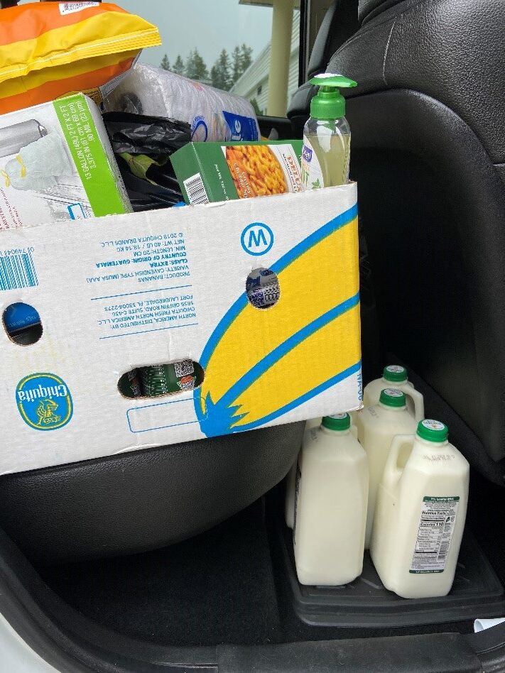 A box full of food and cleaning supplies sits in the back seat of a recipient's car, along with half gallons of milk.
