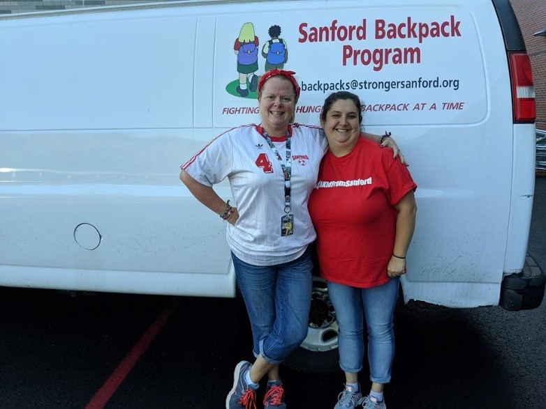 Volunteers stand their van, showing the logo for the Sanford Backpack Program.