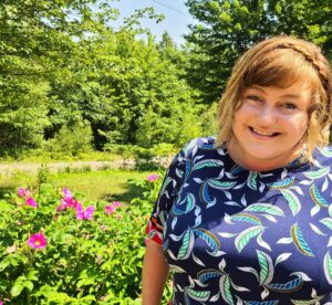 Shannon Coffin smiles in front of wild roses and Maine maple trees.