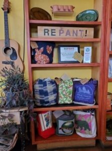 Several colorful Repant! totes displayed on a shelf with a Repant! sign.