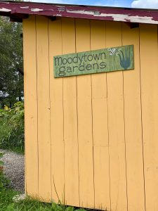 Yellow building with green sign that says Moodytown Gardens with drawing of plant