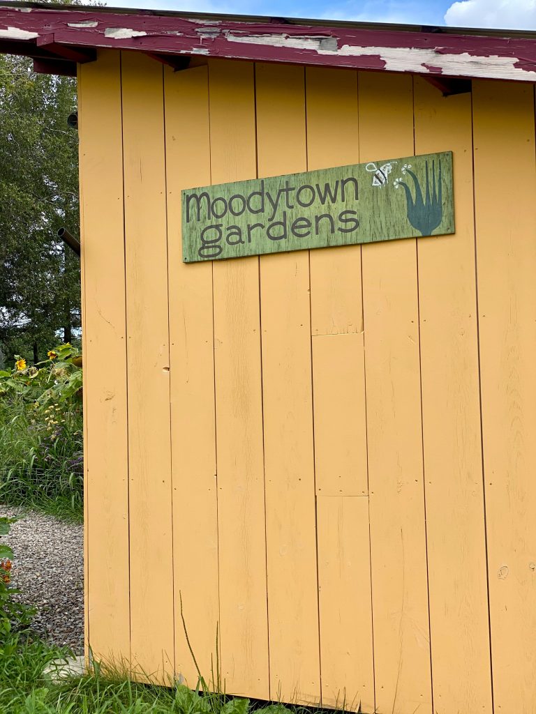 Yellow building with green sign that says Moodytown Gardens with drawing of plant