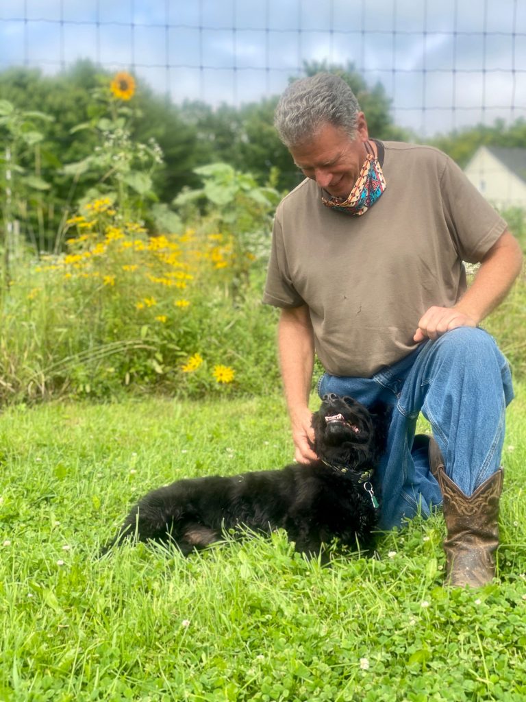 Bill Lombardi and dog kneeling on ground at Sani E Felici Farm in Maine