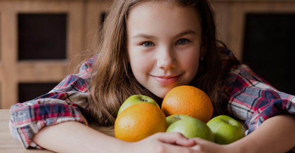Child with plaid shirt hugging oranges and green apples
