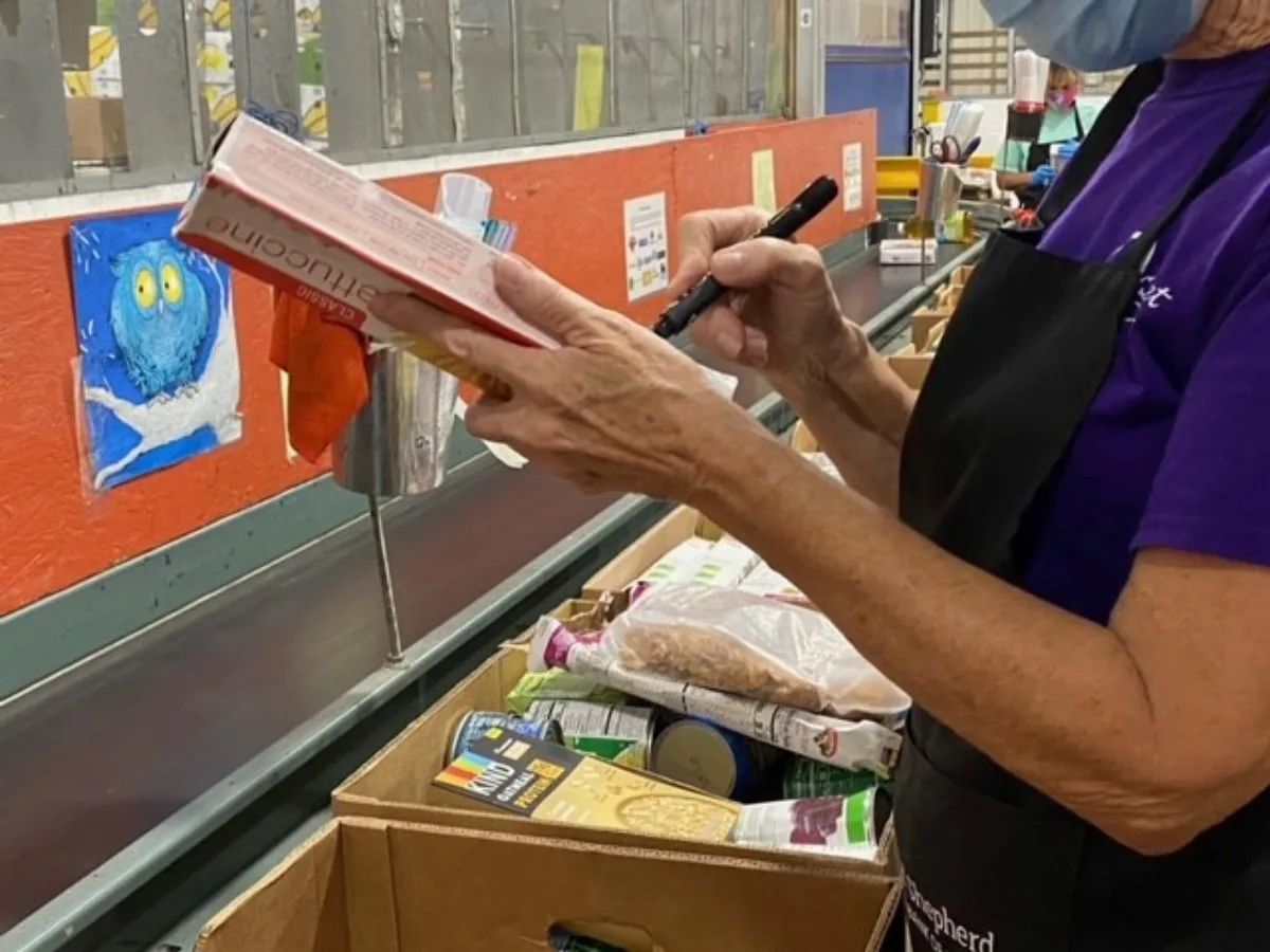 Woman sorting food at Good Shepherd Food Bank of Maine, conveyor belt and box of salvage goods.