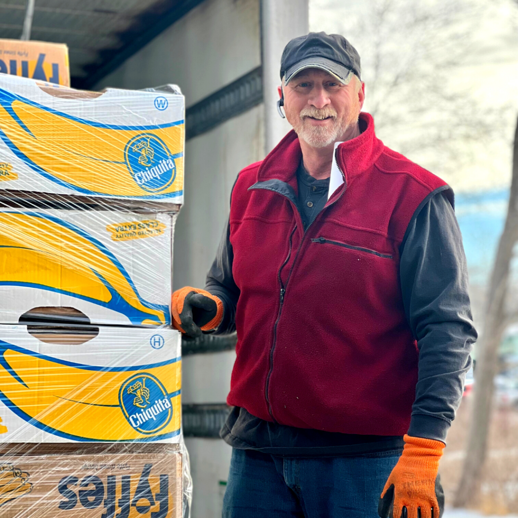 A Good Shepherd Food Bank member smiling with banana boxes.