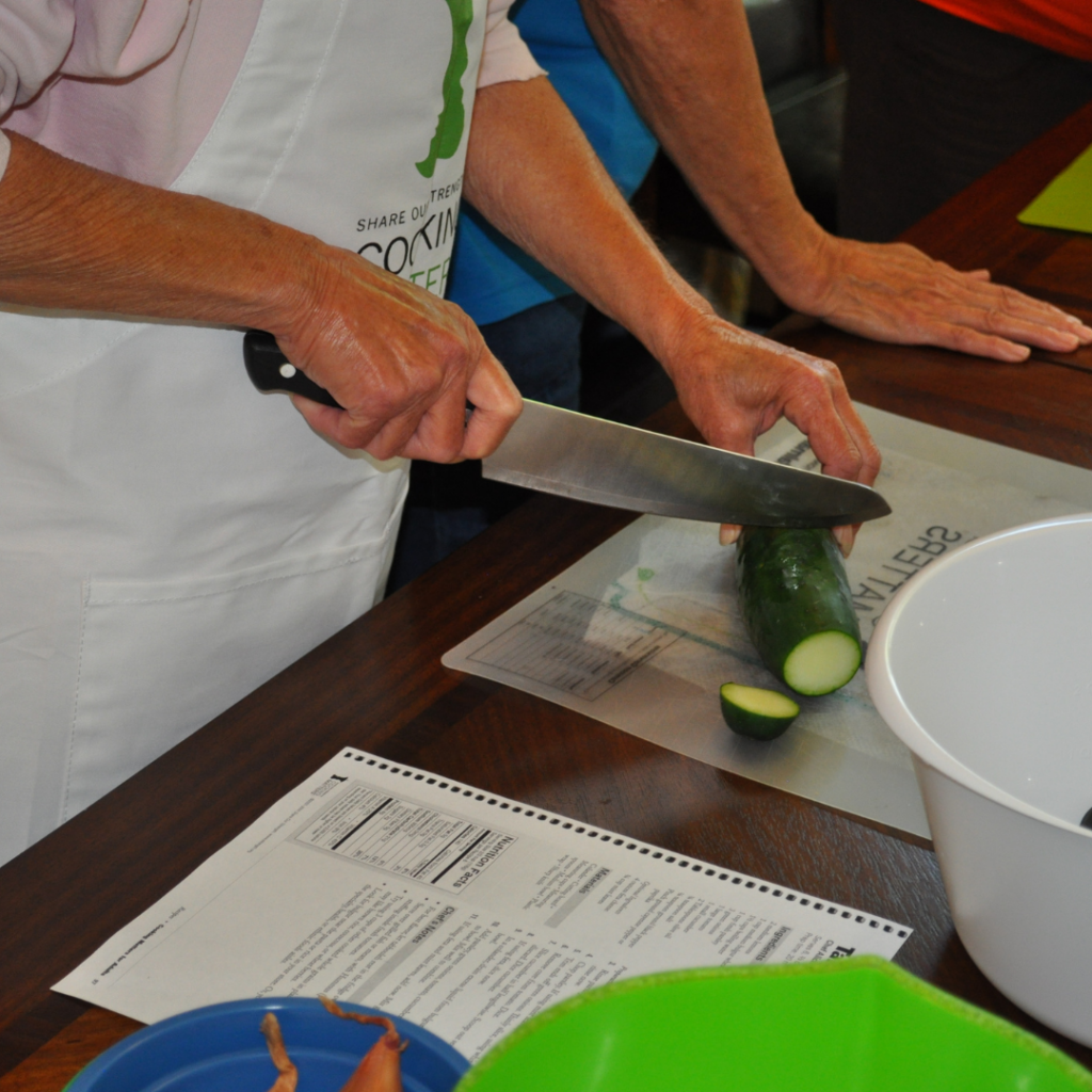 Hands cutting cucumbers on a Cooking Matters mat