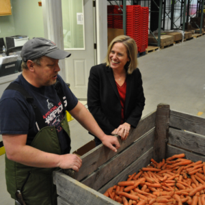 Kristen and team member in warehouse standing in front of bin of carrots