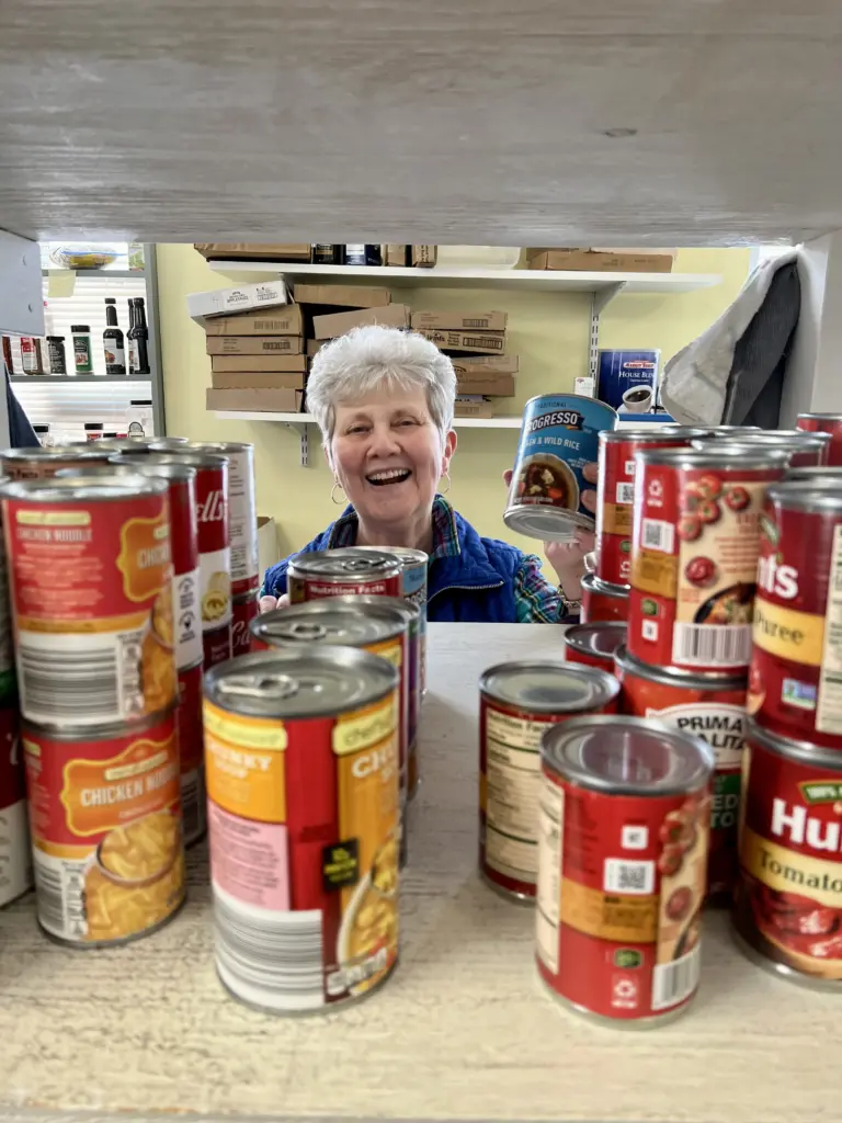 A woman smiles while stocking a shelf with canned food