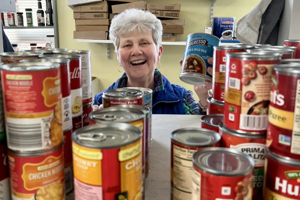 A woman smiles while stocking a shelf with canned food