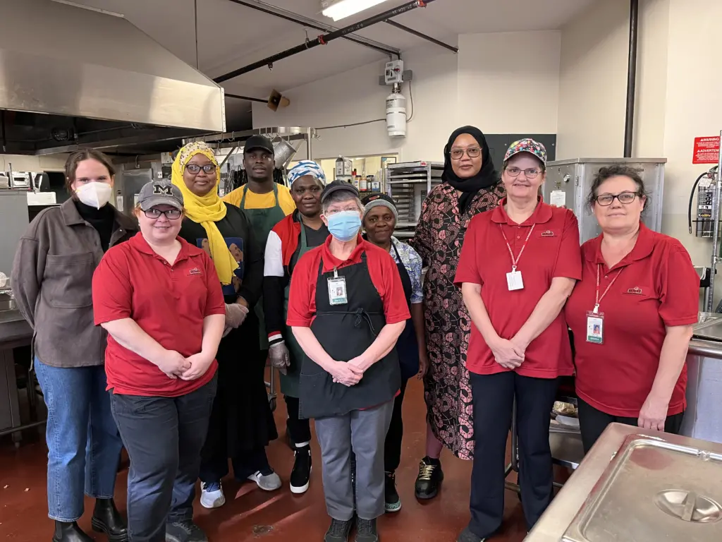 A diverse group of women pose for the camera while standing in a commercial kitchen
