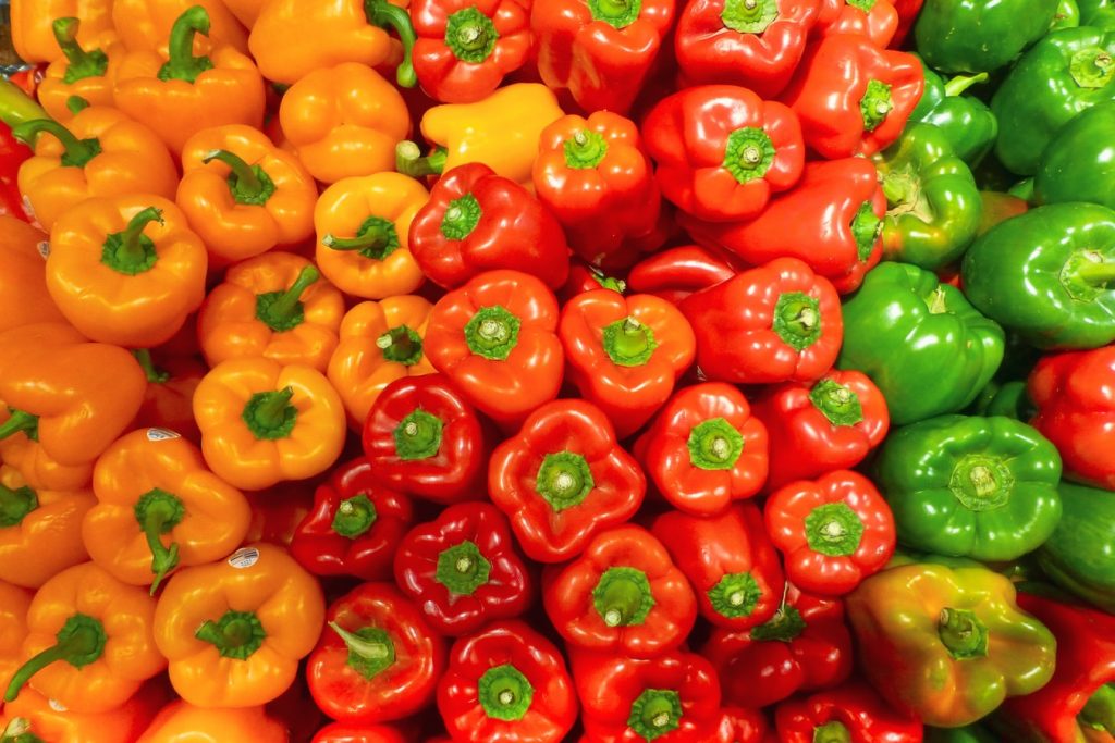 Yellow, orange, red, and green bell peppers lined up on table.