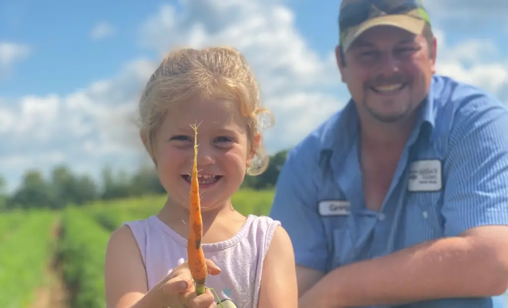 A small child holding a freshly grown carrot with a man smiling 