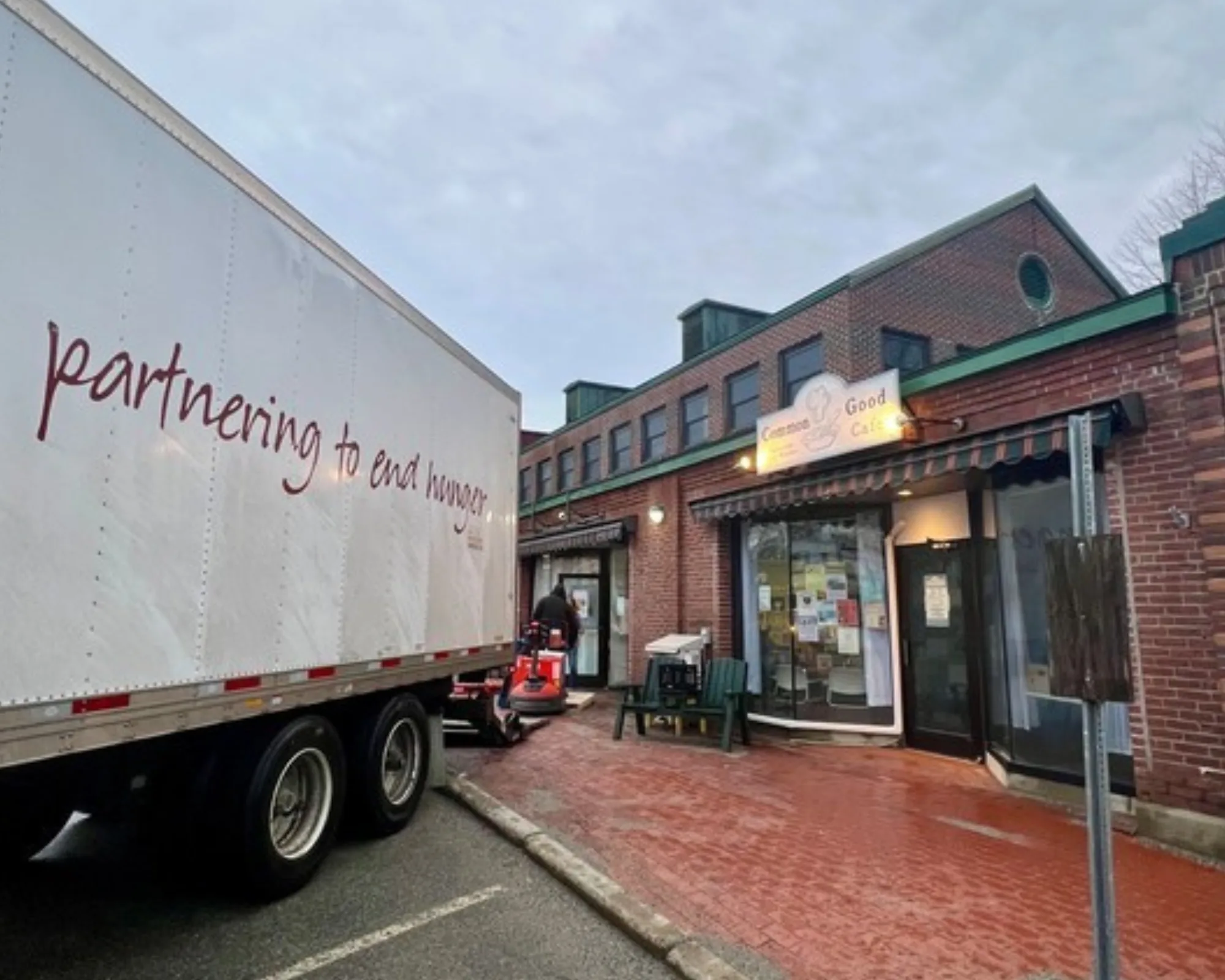 A truck with partnering to end hunger parked outside a brick building with a sign reading Good Cafe near the entrance.