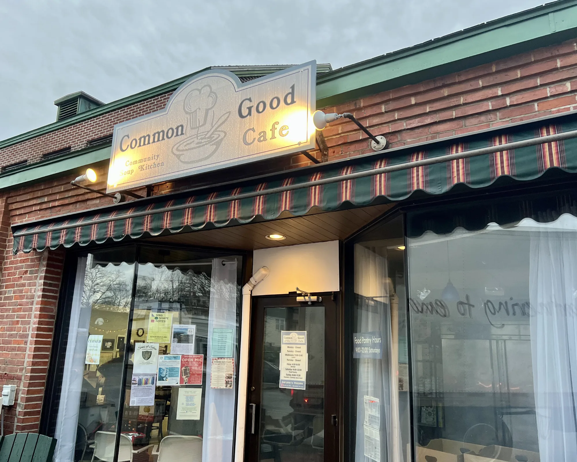 Storefront of Common Good Cafe with a striped awning, glass windows displaying posters, and a sign reading Common Good Cafe above the entrance.