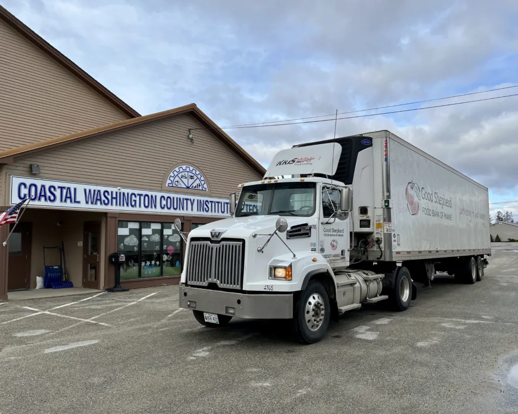 A white semi-truck is parked outside the Coastal Washington County Institute of Technology building on a cloudy day.