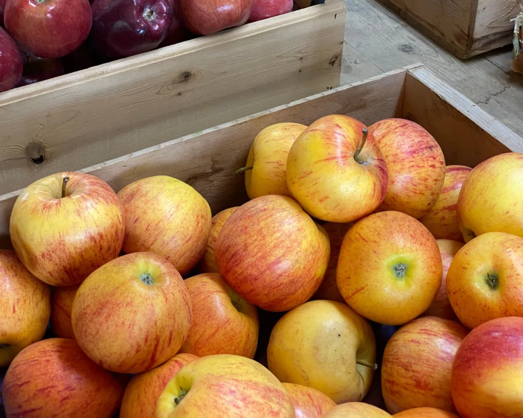 A wooden crate filled with yellow and red apples, with more apples in a crate behind them, displayed at a market.