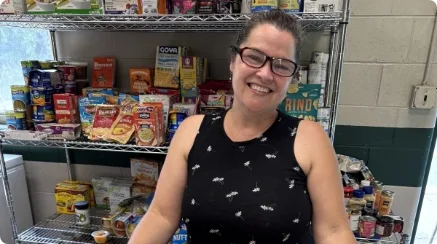 Candice smiles and stands in front of a shelf full of food in the Auburn PAL food pantry.