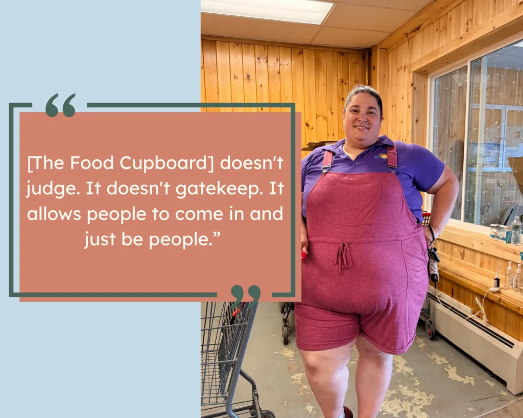 A person in pink overalls and a purple shirt stands by a shopping cart, smiling. Quote: [The Food Cupboard] doesnt judge. It doesnt gatekeep. It allows people to come in and just be people..